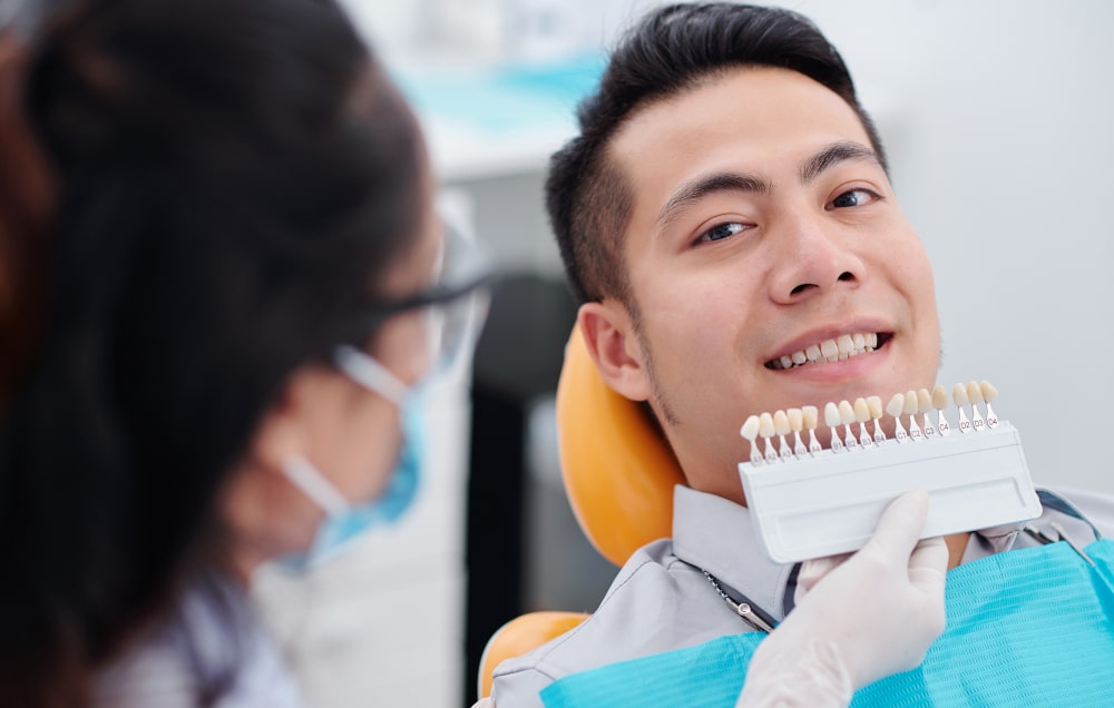 Dentist comparing veneer shades for front teeth in dental office